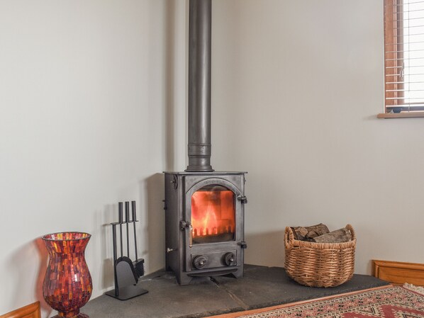 A room with a wood-burning stove, a vase, and a basket of wood. - 1 bedroom accommodation in Bridgend (Bridgend)