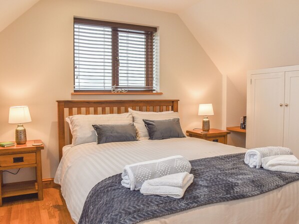Ein Schlafzimmer mit einem großen Bett, zwei Nachttischen, einem Fenster mit Jalousien, einem Kleiderschrank und einer Nachttischlampe.