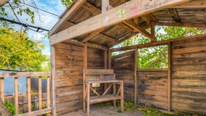 Una estructura rústica de madera con un banco y una mesa, rodeada por una terraza de madera y árboles.