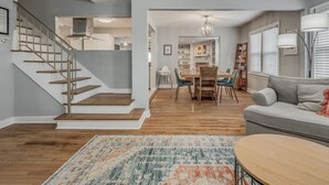 Un salón amplio con una escalera de madera, una mesa de comedor y un sofá gris.