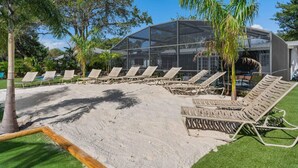 Un área de descanso en la playa con tumbonas, un edificio de cristal y palmeras.