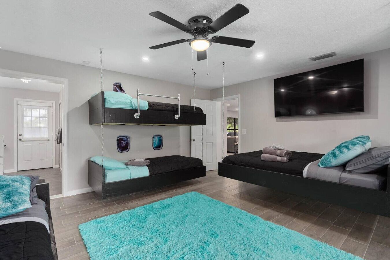 A modern bedroom with bunk beds, a ceiling fan, a large TV, and a bright window.