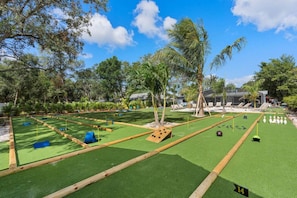 A croquet field with a pool table, lounge chairs, and palm trees.