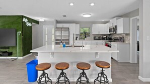 Una cocina moderna con una isla central, taburetes de bar y un televisor de pantalla plana montado en una pared verde.