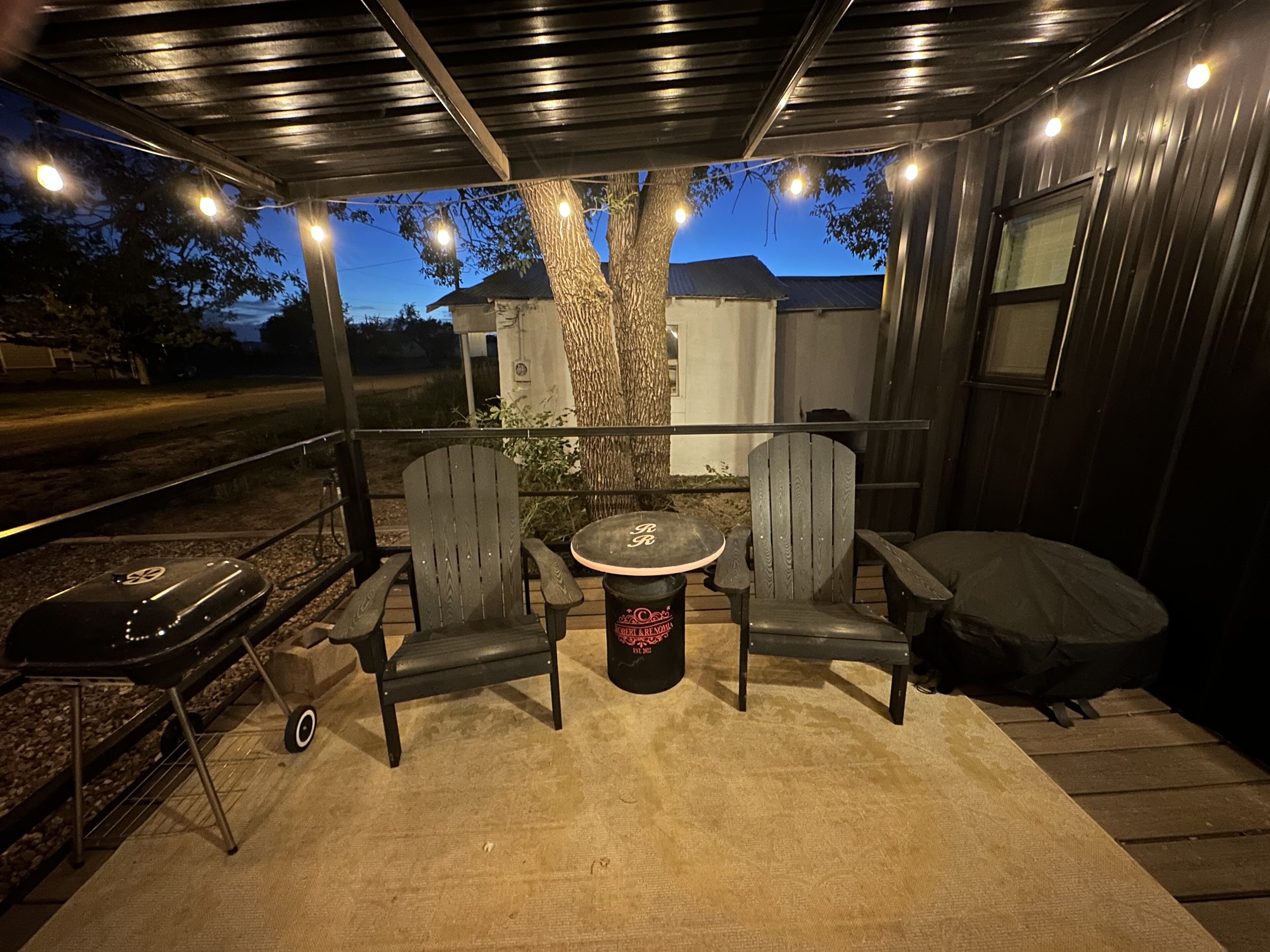 Une terrasse extérieure avec une table ronde et deux chaises, un barbecue et un espace salon abrité.