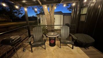 Une terrasse extérieure avec une table ronde et deux chaises, un barbecue et un espace salon abrité.