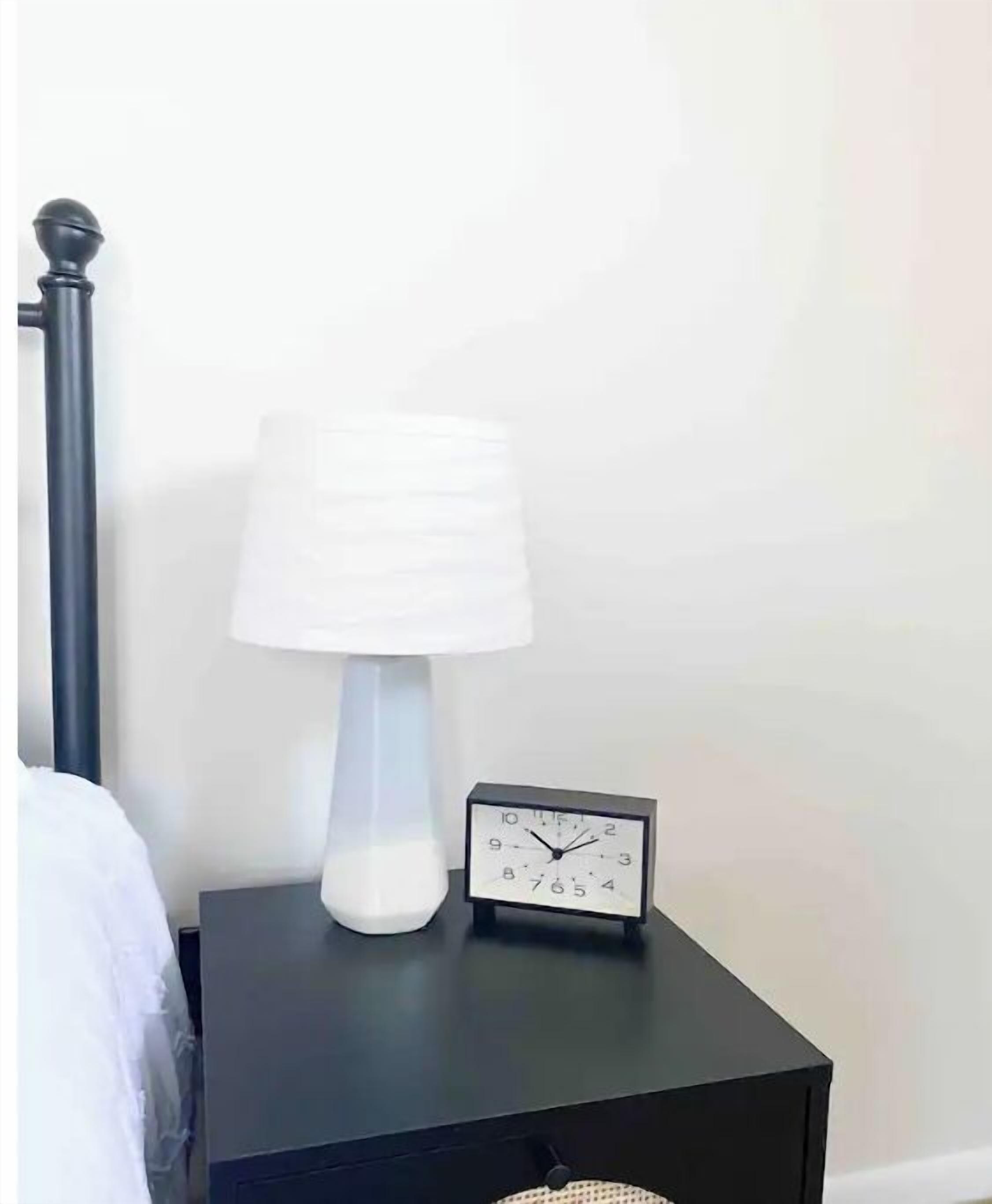 A black bedside table with a white lamp and a small black alarm clock.