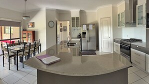 A modern kitchen with a central island, stainless steel appliances, and a dining area with a table and chairs. - Spacious Country Home (Mount Tully)