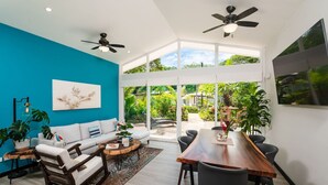 A modern living room with a teal accent wall, a white sofa, a wooden dining table, and a ceiling fan. - Surf, Relax and Explore the best of Avellanas (Playa Avellanas)