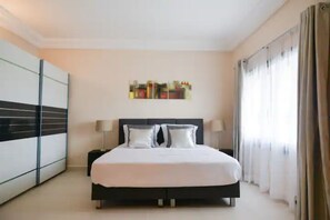 Une chambre à coucher moderne avec un grand lit, des tables de chevet, une armoire et un tableau au mur.
