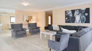 A modern living room with grey sofas, a white coffee table, and a large abstract painting on the wall. - Atlantic Luxury Apartments (Penthouse) (cape point)