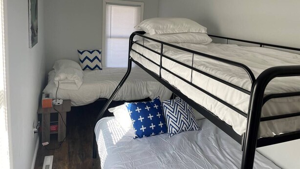 Une chambre de dortoir avec des lits superposés, une fenêtre avec des stores, un petit bureau avec une lampe et une étagère fixée au mur.