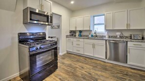 A modern kitchen with stainless steel appliances, white cabinetry, and a wooden floor. - Dunes Home – Walk to Town, Fenced Yard, Near Dunes | Valpo University | Dunes (Chesterton)