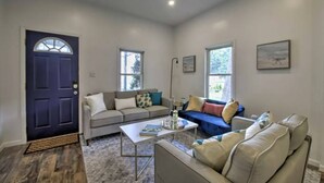 Un salon avec une porte bleu foncé, un canapé gris, un canapé bleu, une table basse et un lampadaire.
