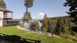 A house with a balcony overlooking a lake, surrounded by trees and a fenced yard. - Coeur d'Alene Lake House - Hot Tub with lake view, beach/lake access/boat launch (Worley)