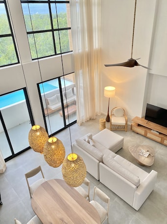 A modern living room with a large window, a sofa, a TV, and a dining area.