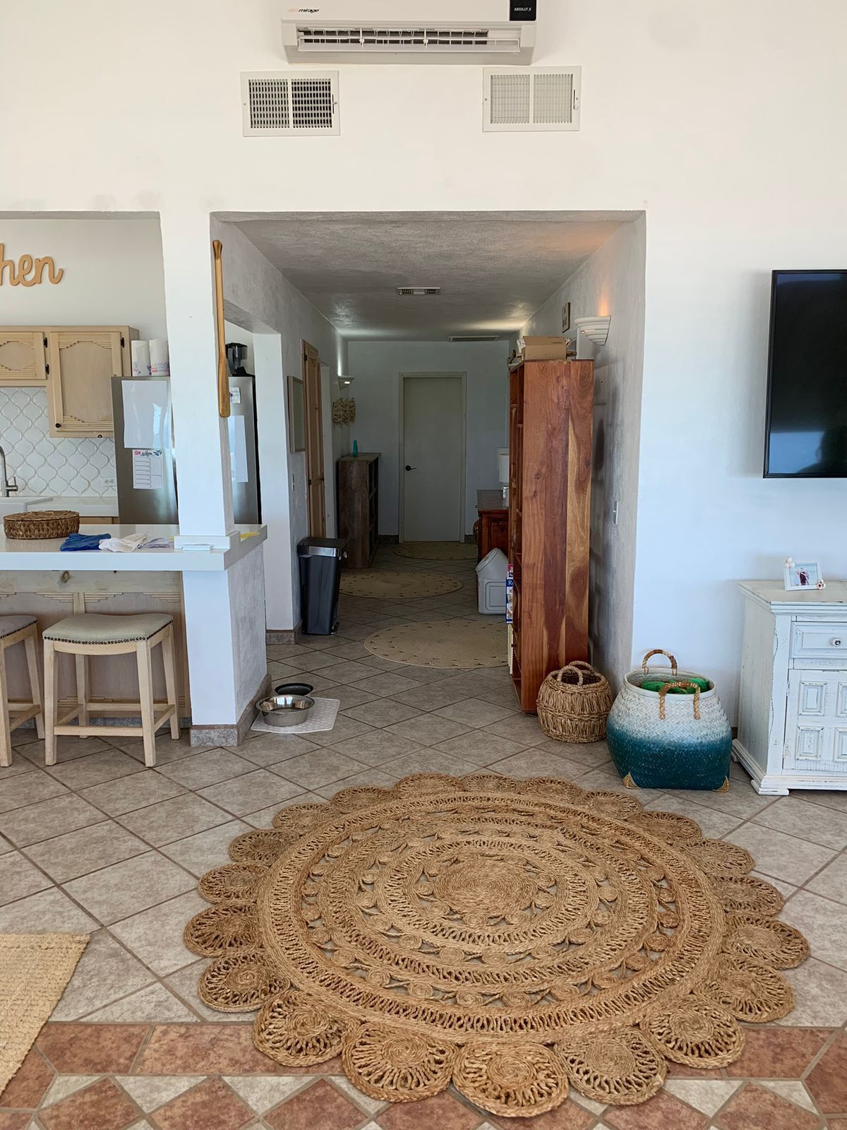 Une cuisine avec un plan de travail blanc, des tabourets en bois, un tapis tissé et un meuble en bois.