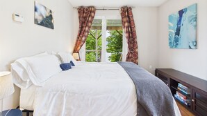 Ein Schlafzimmer mit einem Bett, einem Fenster mit Vorhängen, einem Gemälde und einem Bücherregal.