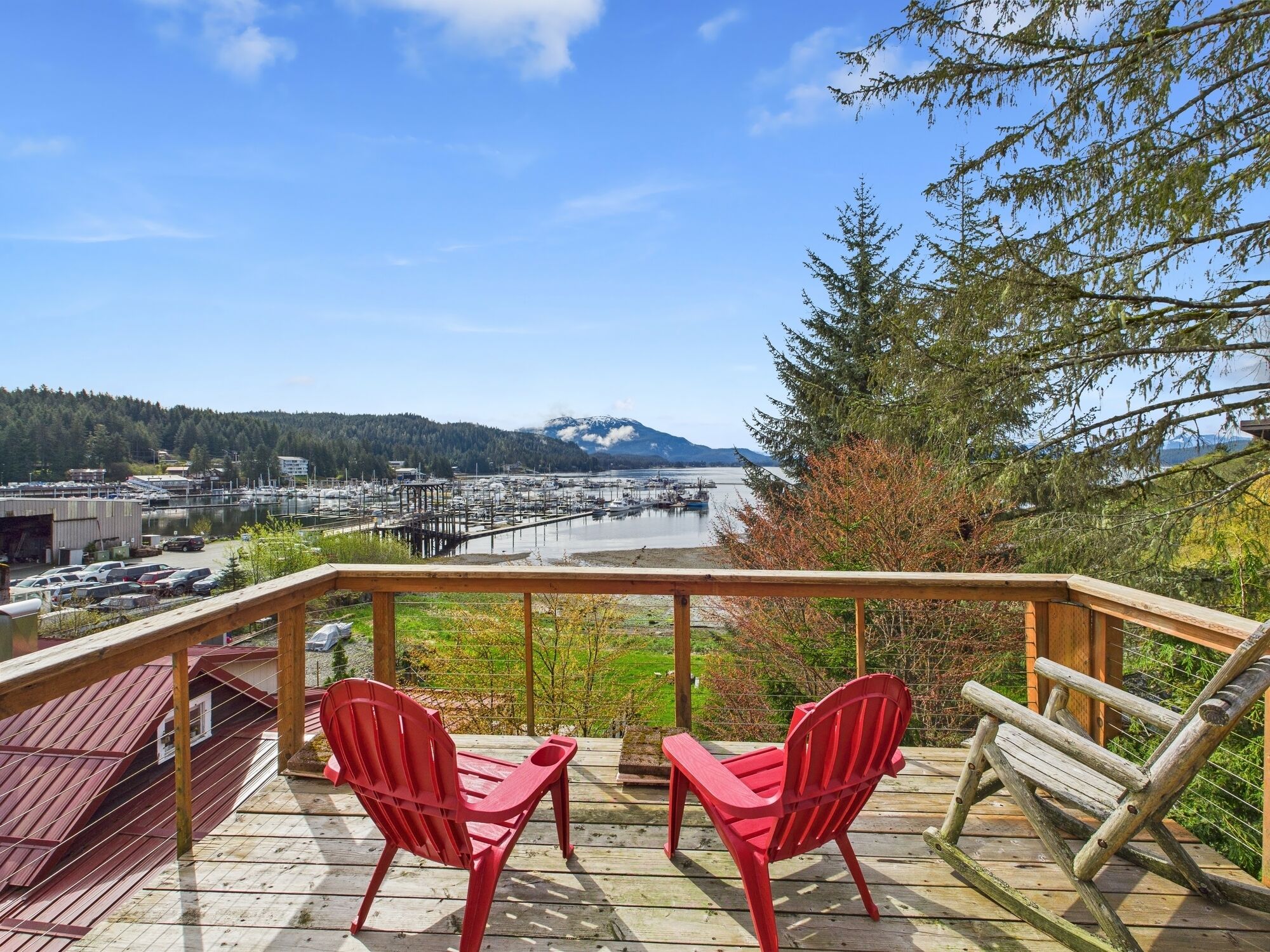 A wooden deck with two red Adirondack chairs overlooking a marina and mountains.