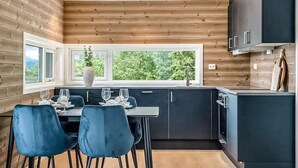 A modern kitchen with wooden paneling, a dining area with blue chairs, and a window with a view of greenery. - Awesome home in Gjemnes with WiFi (Gjemnes)