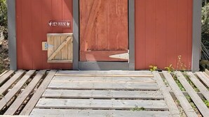 Una pequeña estructura de madera roja con una sola puerta, dos ventanas y un portón de madera.
