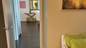 A hallway leading to a room with a green pillow on a white bed, a painting on the wall, and a kitchen area in the background. - Eloquently decorated 1 bedroom, 1 1/2  bath condo. Beautiful water views/balcony (West Palm Beach)