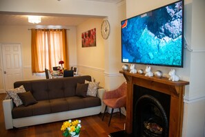 A living room with a sofa, a fireplace, a TV, and a dining area in the background.