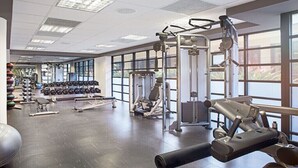 Un gimnasio con diversos equipos de ejercicio, amplias ventanas y un espacio amplio.