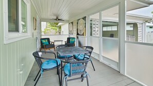 Un patio couvert avec une table et des chaises, un ventilateur de plafond et une vue sur le jardin arrière.