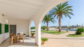 A covered outdoor area with a table and chairs, palm trees, and a view of a pool. - YourHouse Goet, villa with private pool (Sa Pobla)