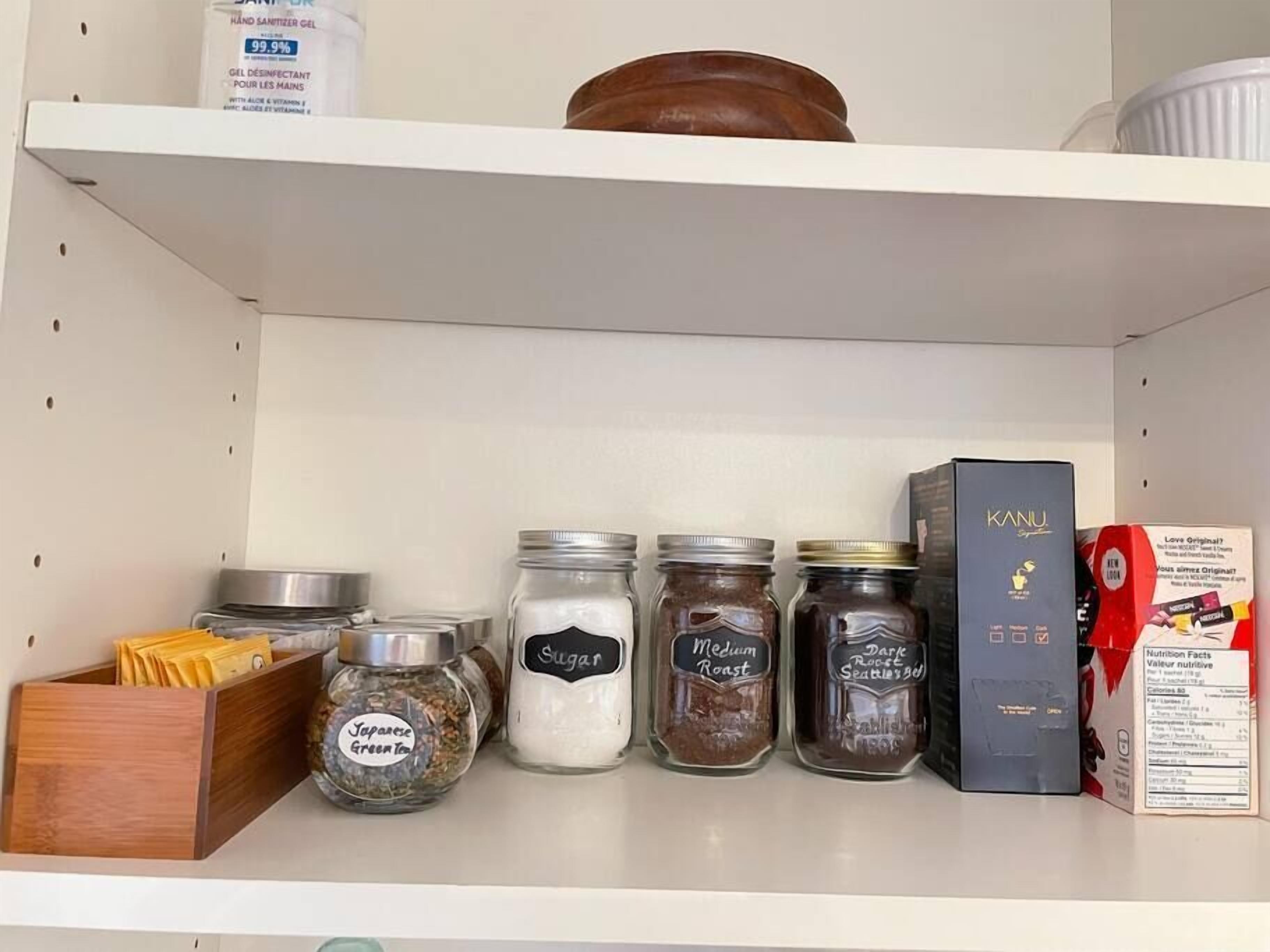 Une étagère de cuisine avec divers pots d’épices, une boîte de chocolats Kanu et une boîte de JELLO.