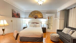 Une chambre d’hôtel comprenant un lit, un bureau, une chaise, un canapé, un ventilateur et une porte donnant accès à une salle de bain.