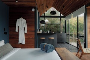 Un dormitorio moderno con una cama grande, techo de madera, bata colgada en la pared y vistas al exterior a través de amplias ventanas.