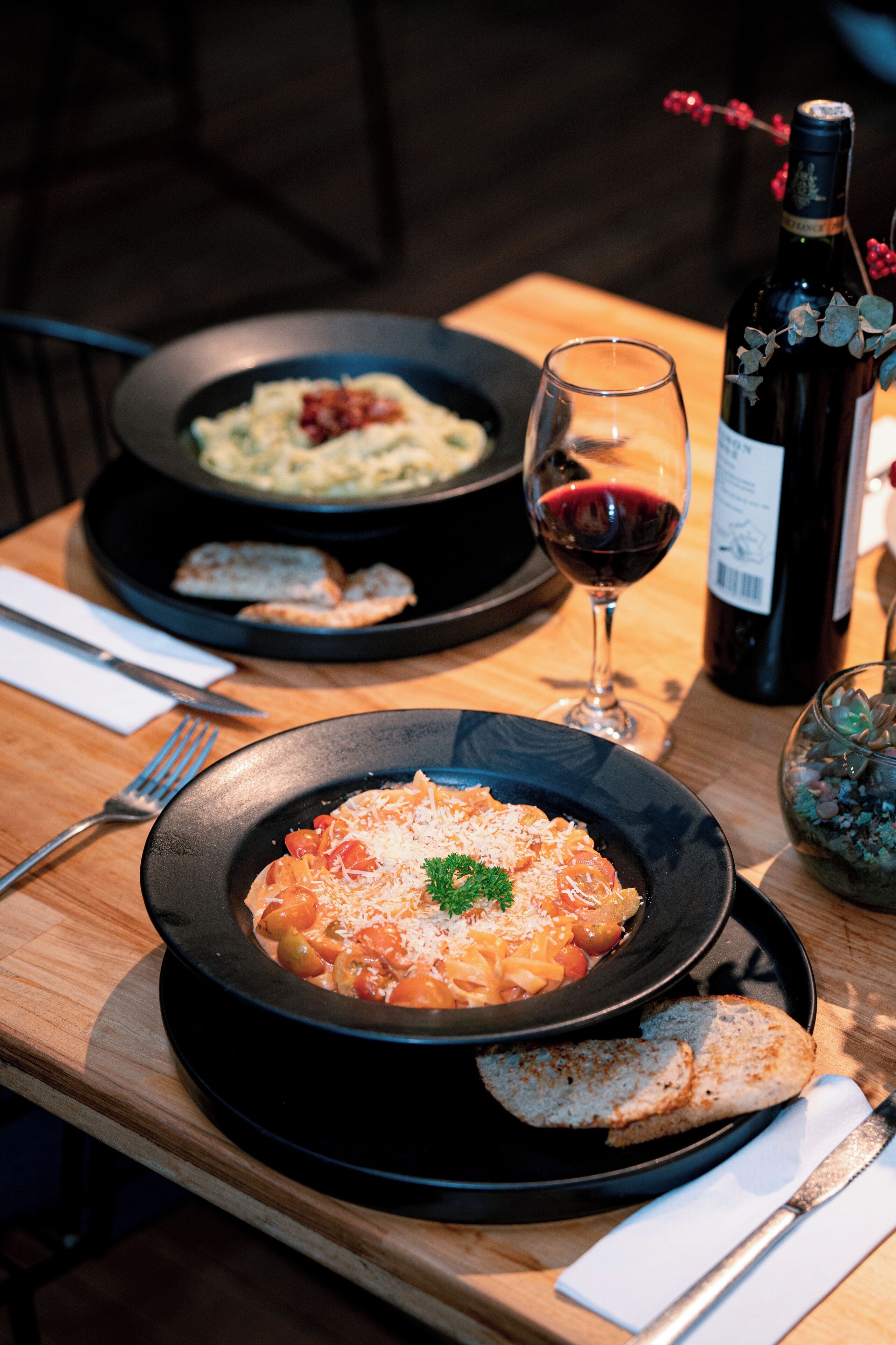 Una mesa de comedor con dos platos de pasta, una copa de vino y una botella.