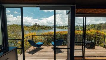 Una habitación moderna con ventanas amplias, una terraza de madera y vistas a un lago y bosque.