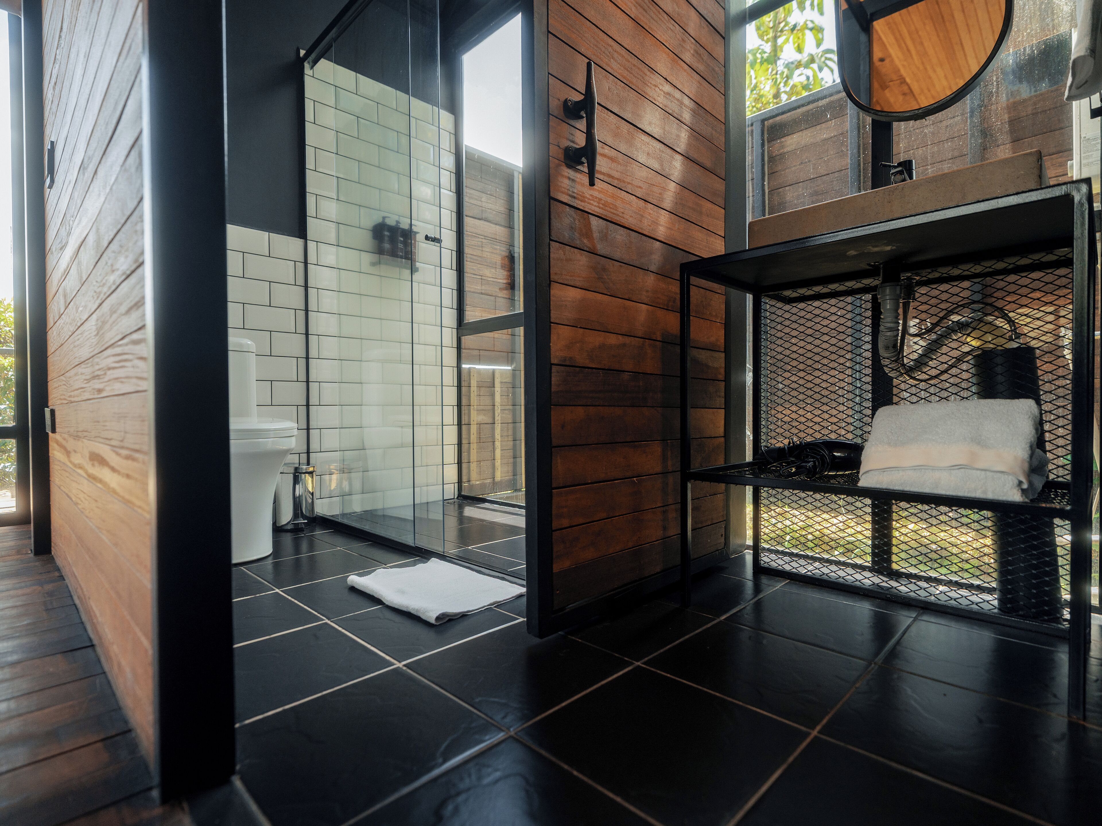 A modern bathroom with a glass shower enclosure, a wooden wall, and a black tiled floor.