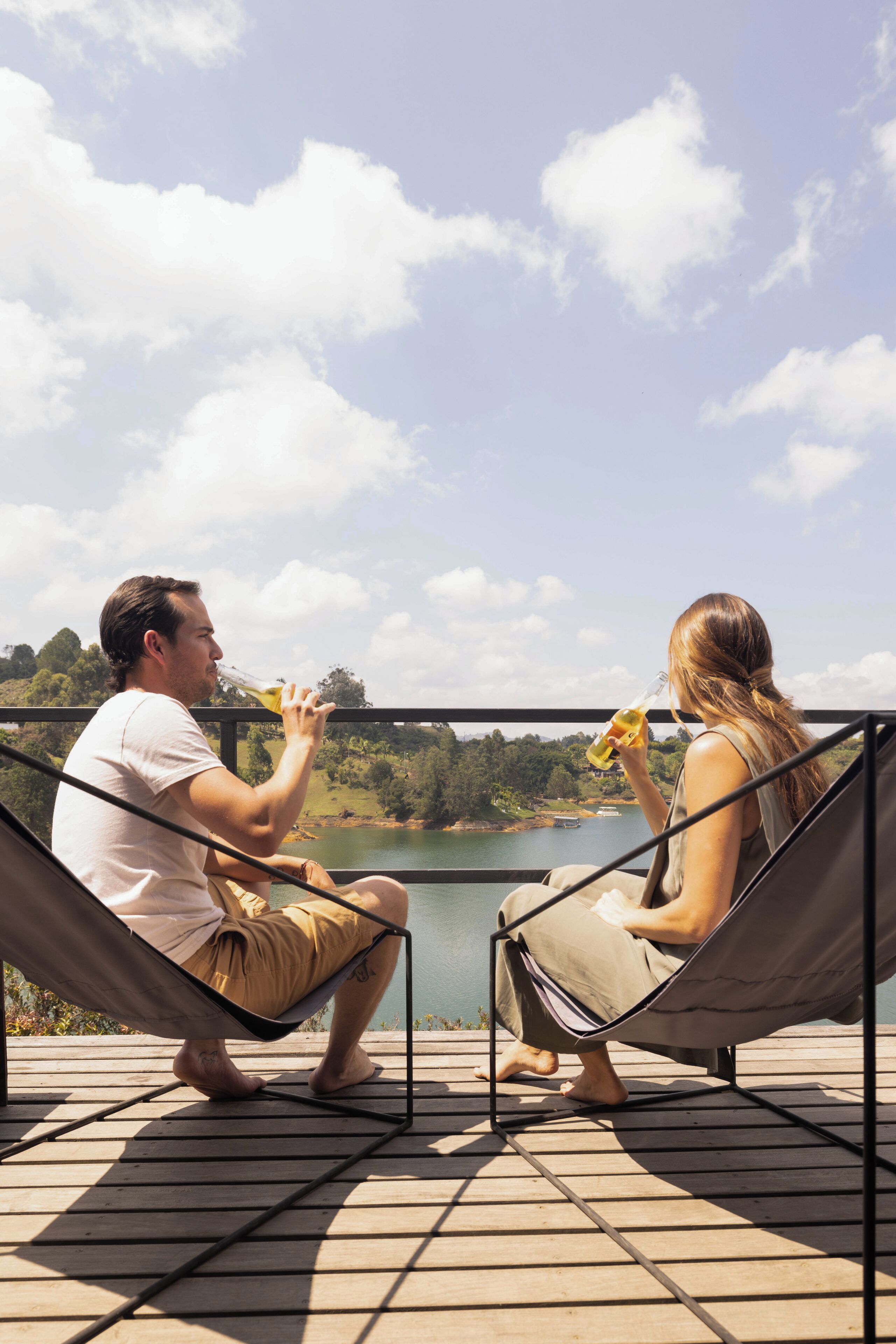 Two people sitting in hammocks on a deck overlooking a lake.