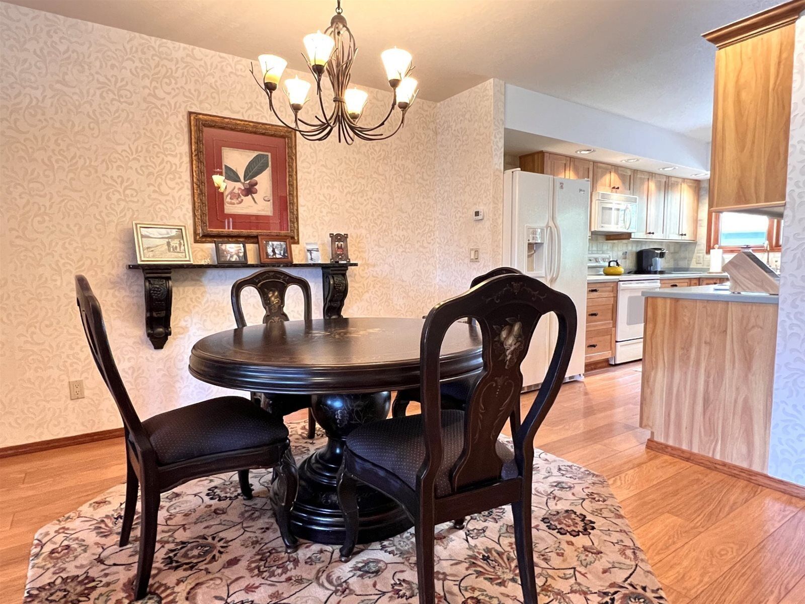 A dining area with a round table and chairs, a chandelier, and a floral-patterned rug.