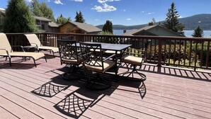 Una terraza de madera con una mesa y sillas, con vista a un lago y montañas.