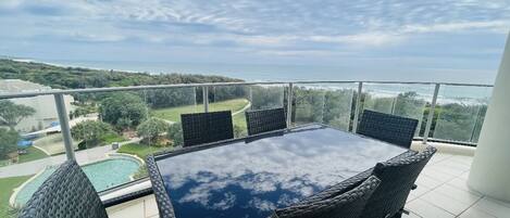 Enjoy a serene coastal view from this balcony with a glass-top table and comfortable wicker chairs.