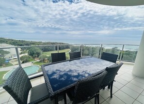 Enjoy a serene coastal view from this balcony with a glass-top table and comfortable wicker chairs.
