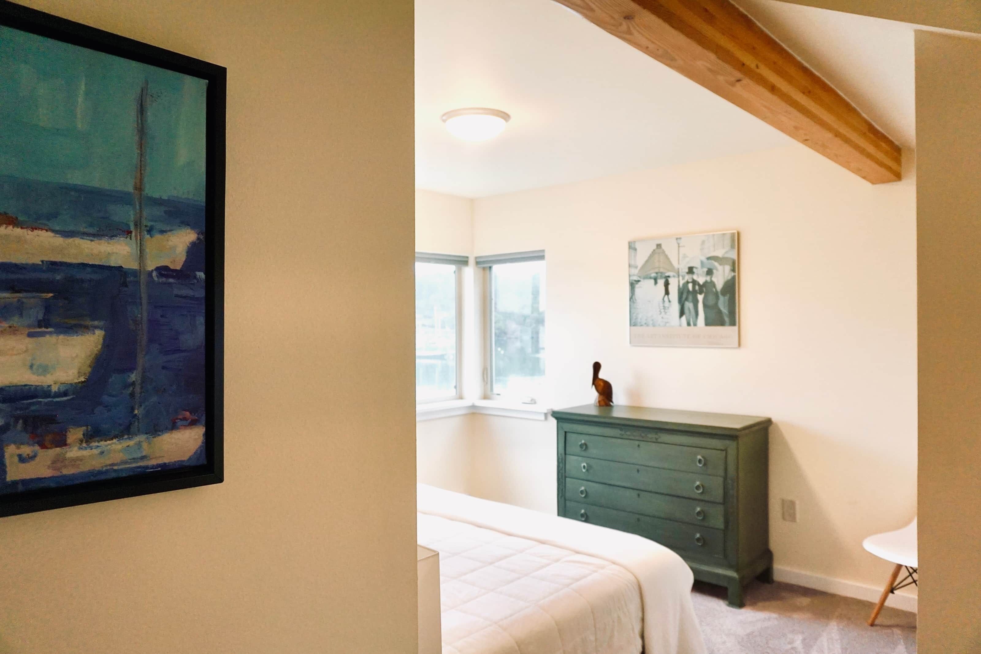 Ein Schlafzimmer mit einem Bett, einem Schminktisch, einem Gemälde und einem Fenster.