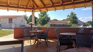 An outdoor patio with wooden tables and chairs, a brick wall, and a view of houses and cars in the background. - Awesome home in Lisane Tinjske (Lisane Tinjske)