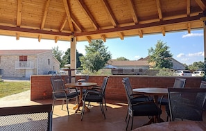 An outdoor patio with wooden tables and chairs, a brick wall, and a view of houses and cars in the background.