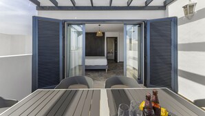 A balcony with a table, two chairs, and a view into a bedroom with a bed and a hanging light fixture. - wema alto (Playa Blanca)