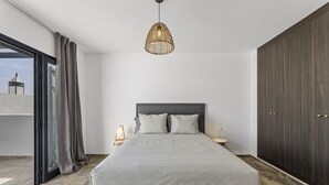 A modern bedroom with a large bed, a hanging light fixture, a wardrobe, and a view through a glass door. - wema alto (Playa Blanca)