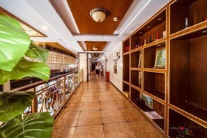 A hotel corridor with a tiled floor, a bar area with a railing, and wooden shelving units with framed pictures. - Ru Jiang Hotel (Zhong County)