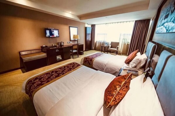 Habitación de hotel con dos camas, un escritorio, una silla, un televisor y una ventana con cortinas.