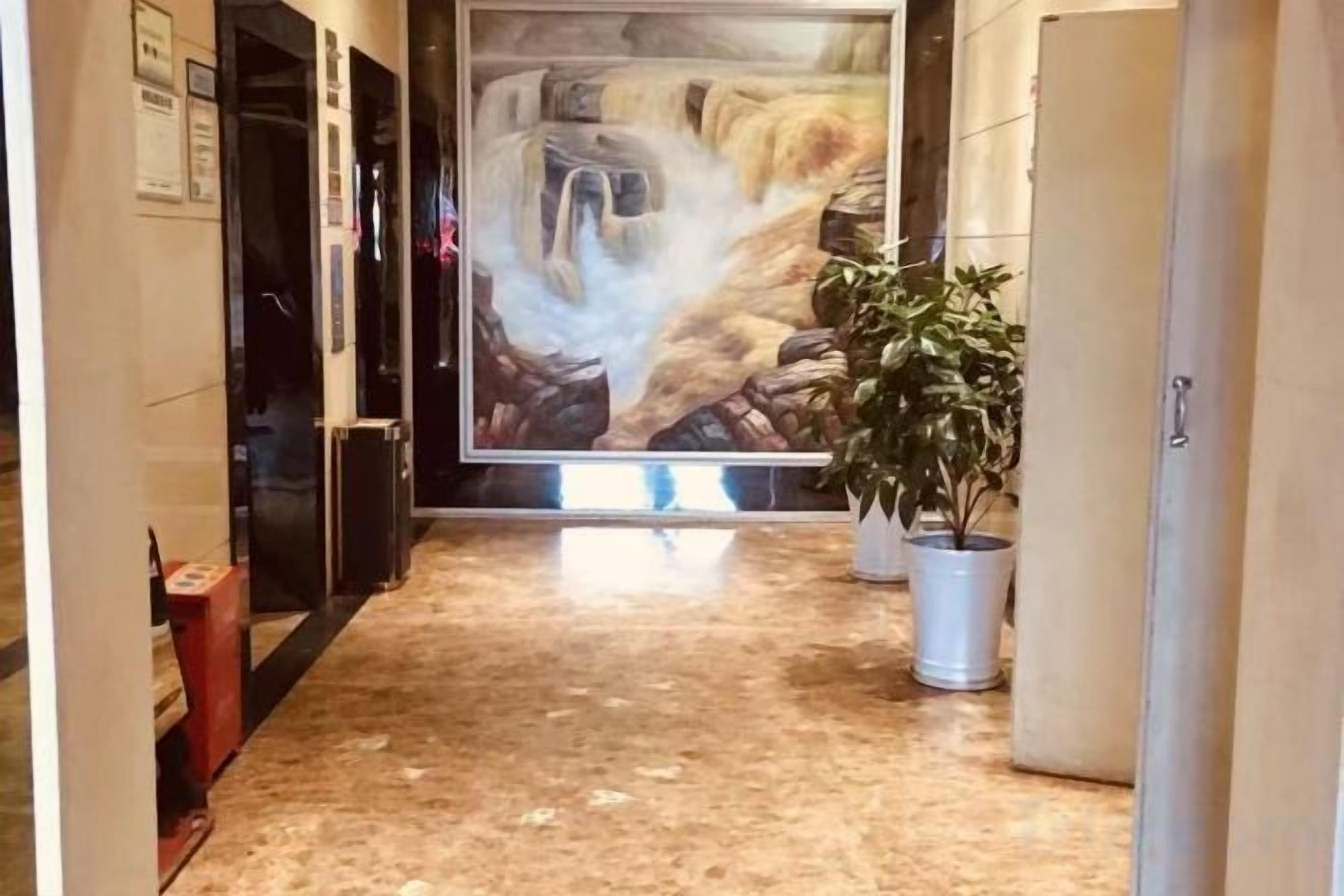 A hallway with a marble floor, a large painting on the wall, and potted plants.