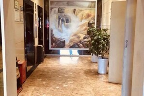 A hallway with a marble floor, a large painting on the wall, and potted plants.
